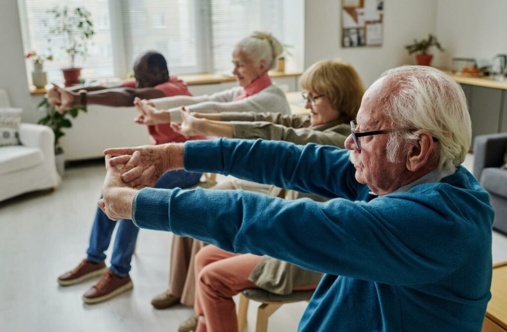 A group of older adults stretch their arms outward during a sitting tai chi session.