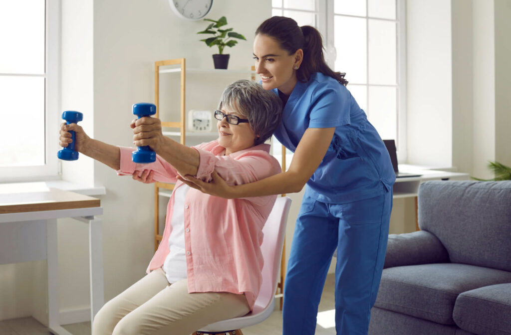 A caregiver smiles while helping a resident in senior living lift small weights to strengthen their arms